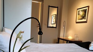 A hotel room with a bed, a bedside table with a lamp, a small table with a glass, a mirror, and a framed picture on the wall. - Rum i Centrum (Vetlanda)