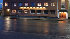 A multi-story building with illuminated windows and a wet street in front. - Rum i Centrum (Vetlanda)