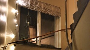 A staircase with a handrail, a window with a geometric patterned valance, and string lights. - Rum i Centrum (Vetlanda)