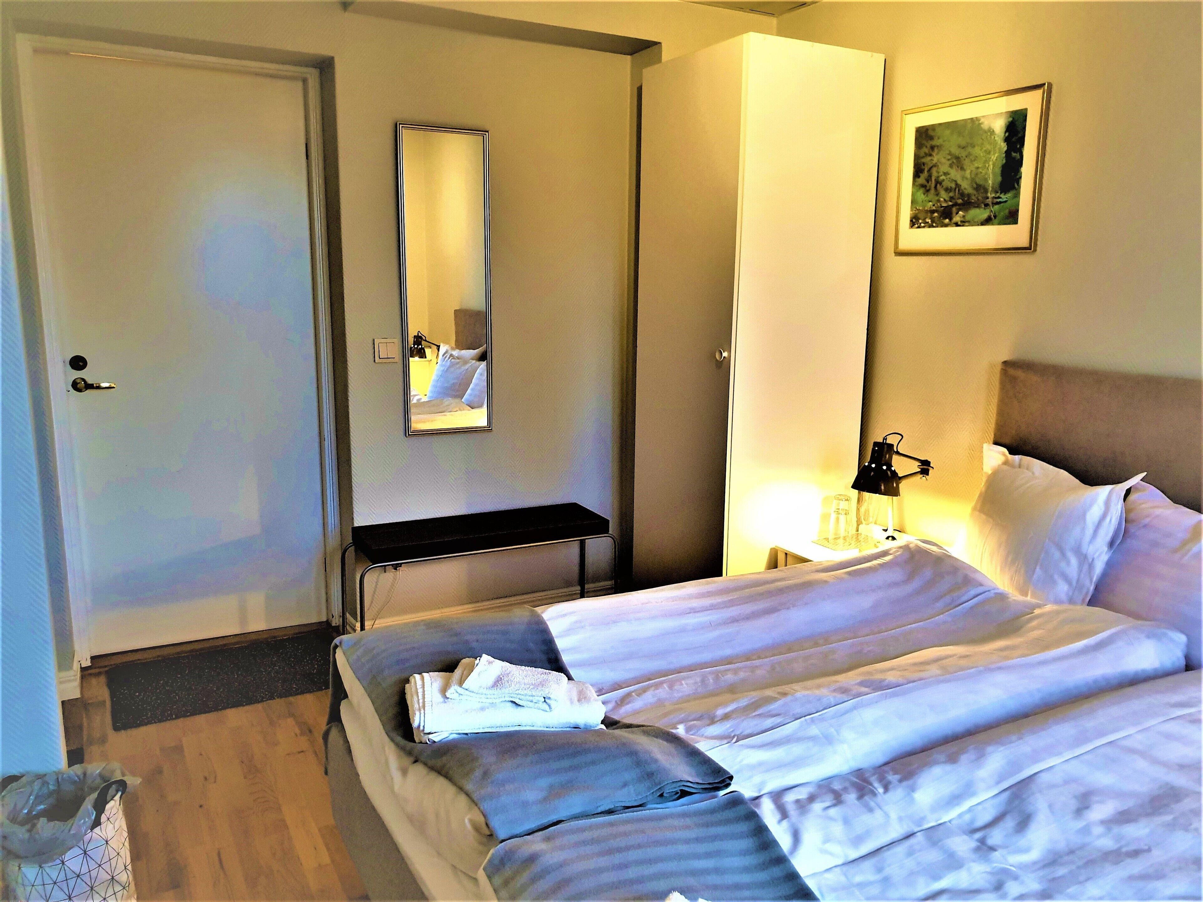 A hotel room with a bed, a bedside table, a mirror, a lamp, and a picture on the wall.