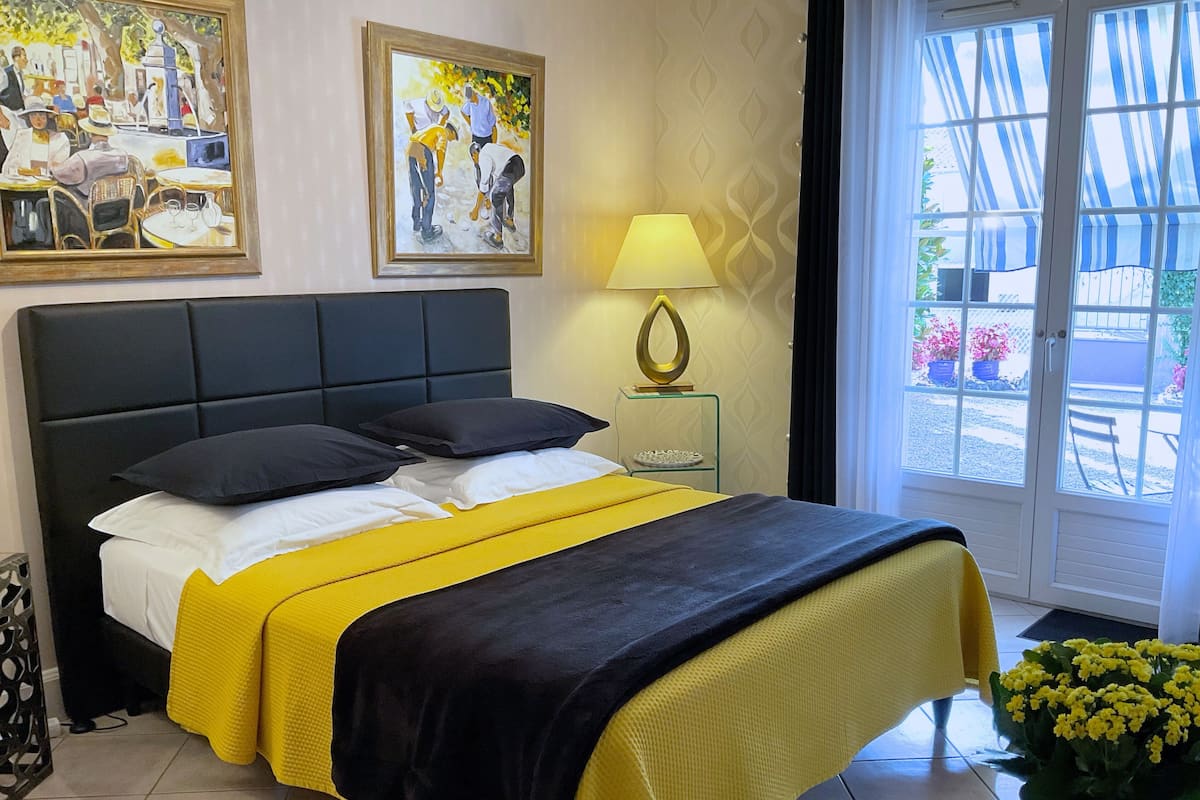 A hotel room with a bed, a nightstand with a lamp, and a window with a view of the outside.