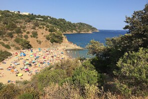 A beach with numerous umbrellas and people, surrounded by hills and trees.
