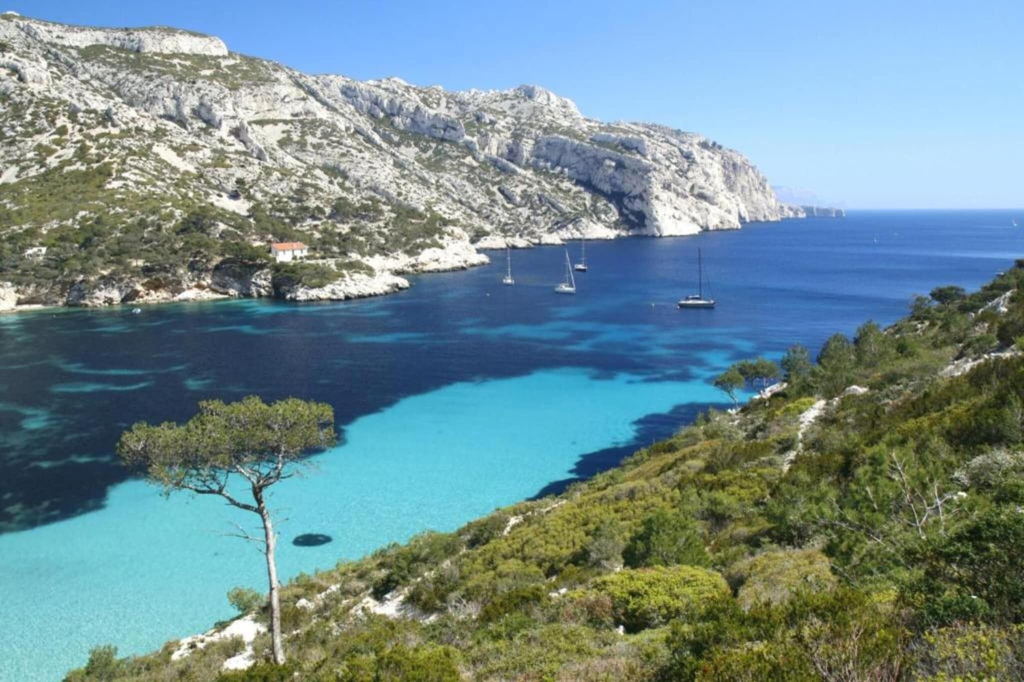 A coastal landscape with clear blue waters, rocky cliffs, and sparse vegetation.
