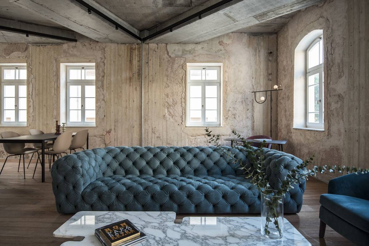 A room with a large tufted sofa, a marble coffee table, and a dining area with chairs and a table.