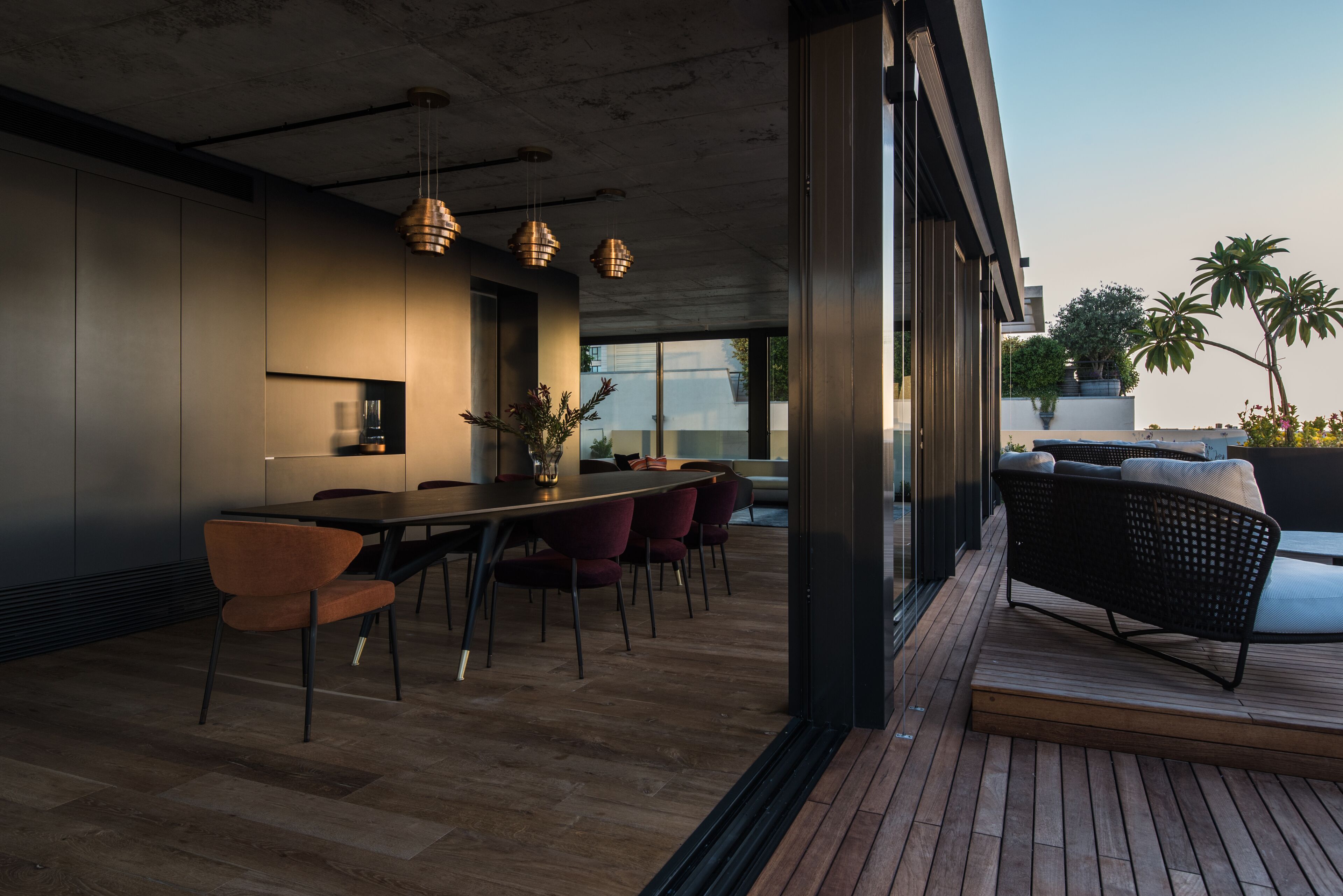 Un espace de restauration moderne avec une longue table, des chaises rouges, des luminaires suspendus et une vue sur l’extérieur.