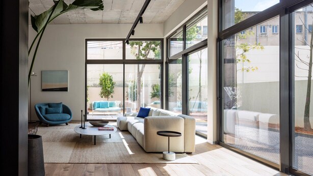 A modern living room with a sofa, a round coffee table, and a large window offering a view of the outdoors.
