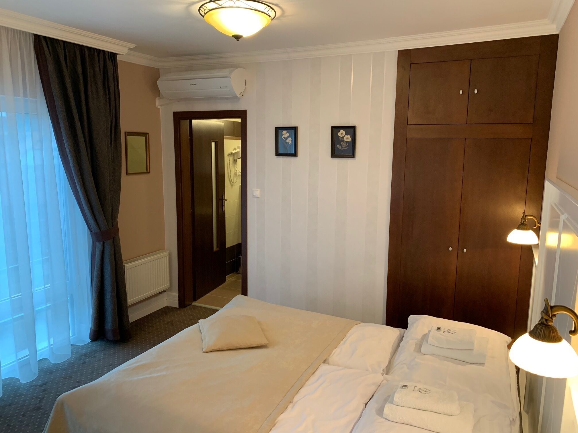 Hotelkamer met een bed, een kledingkast, een badkamer zichtbaar door een geopende deur en een wandlamp.