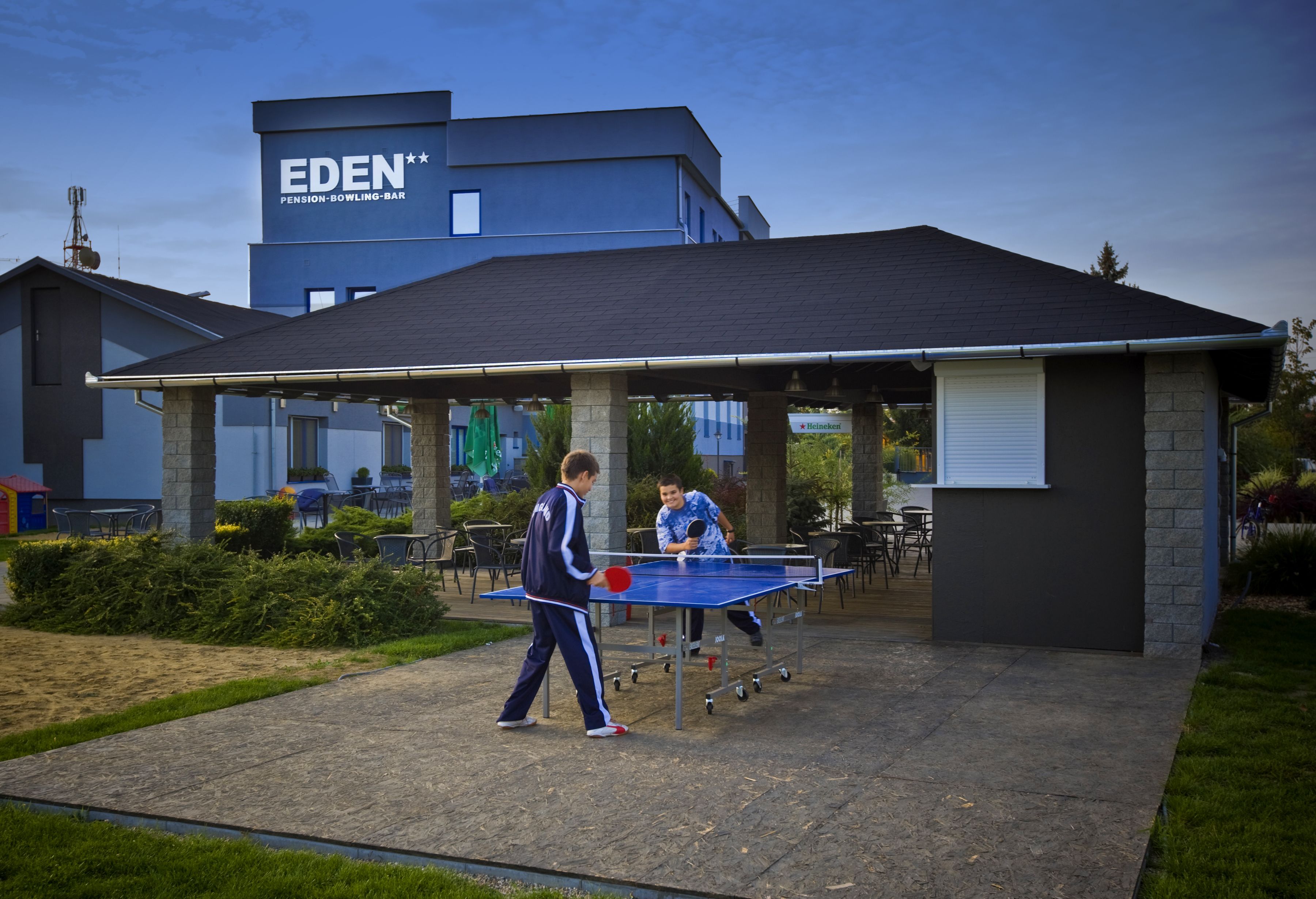 Ein Tischtennistisch vor einem Gebäude, an dem ein Schild mit der Aufschrift 'EDEN Pension-Bowling-Bar' hängt.