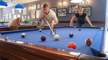 Een pooltafel met ballen en stokken, omringd door ingelijste foto's aan de muur.