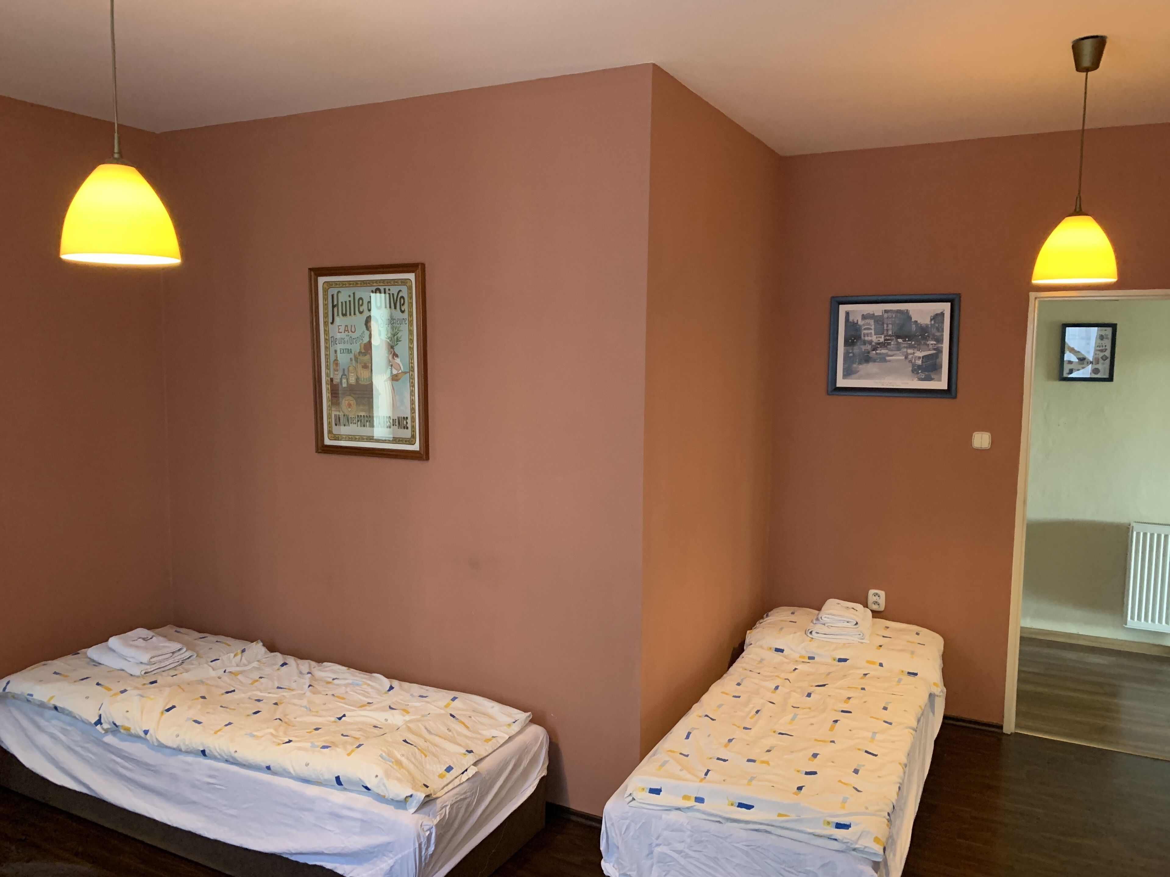 A room with two single beds, a framed picture on the wall, and a door leading to a bathroom.