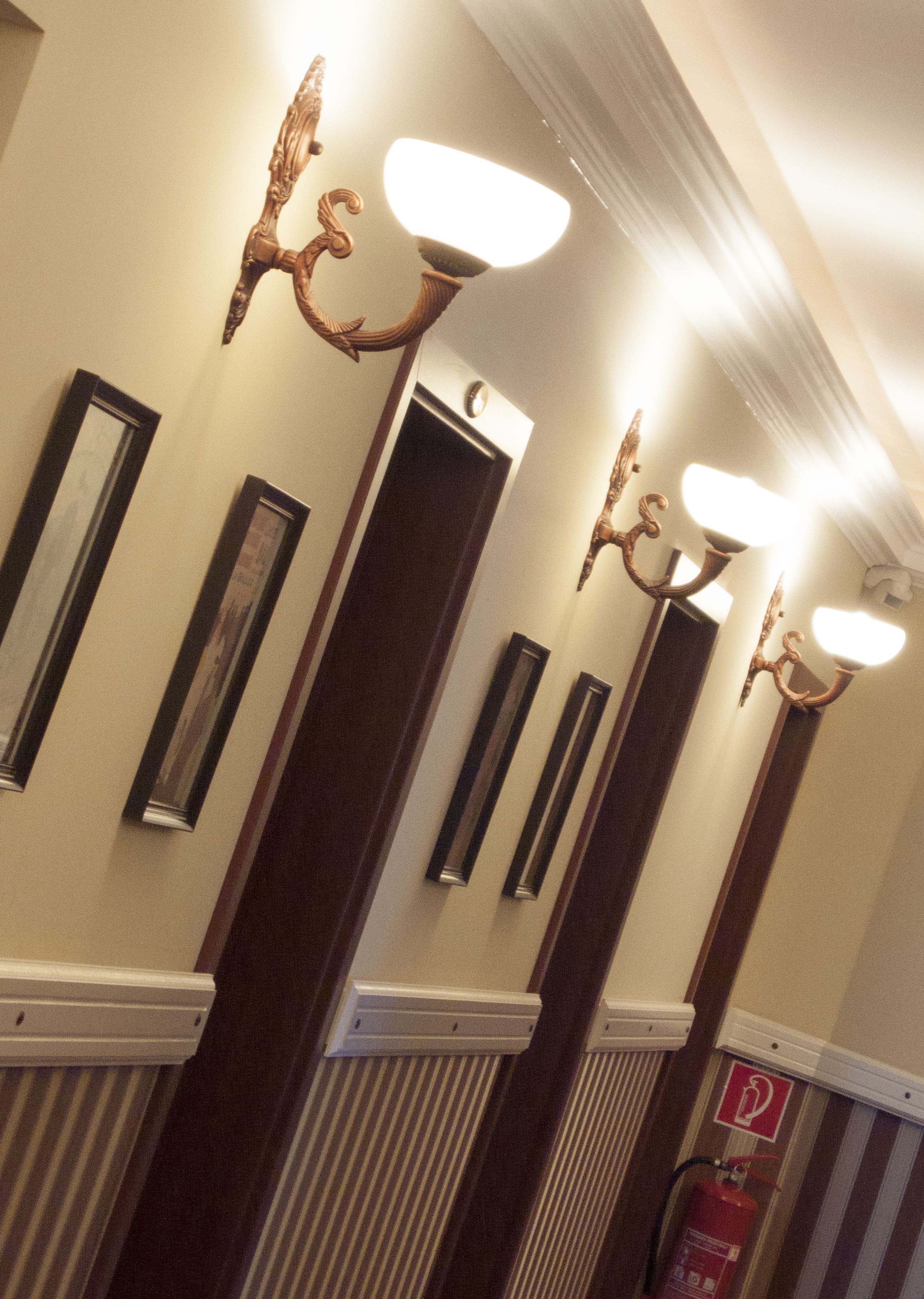 A hallway with wall-mounted sconces, a fire extinguisher, and a door with a handle.