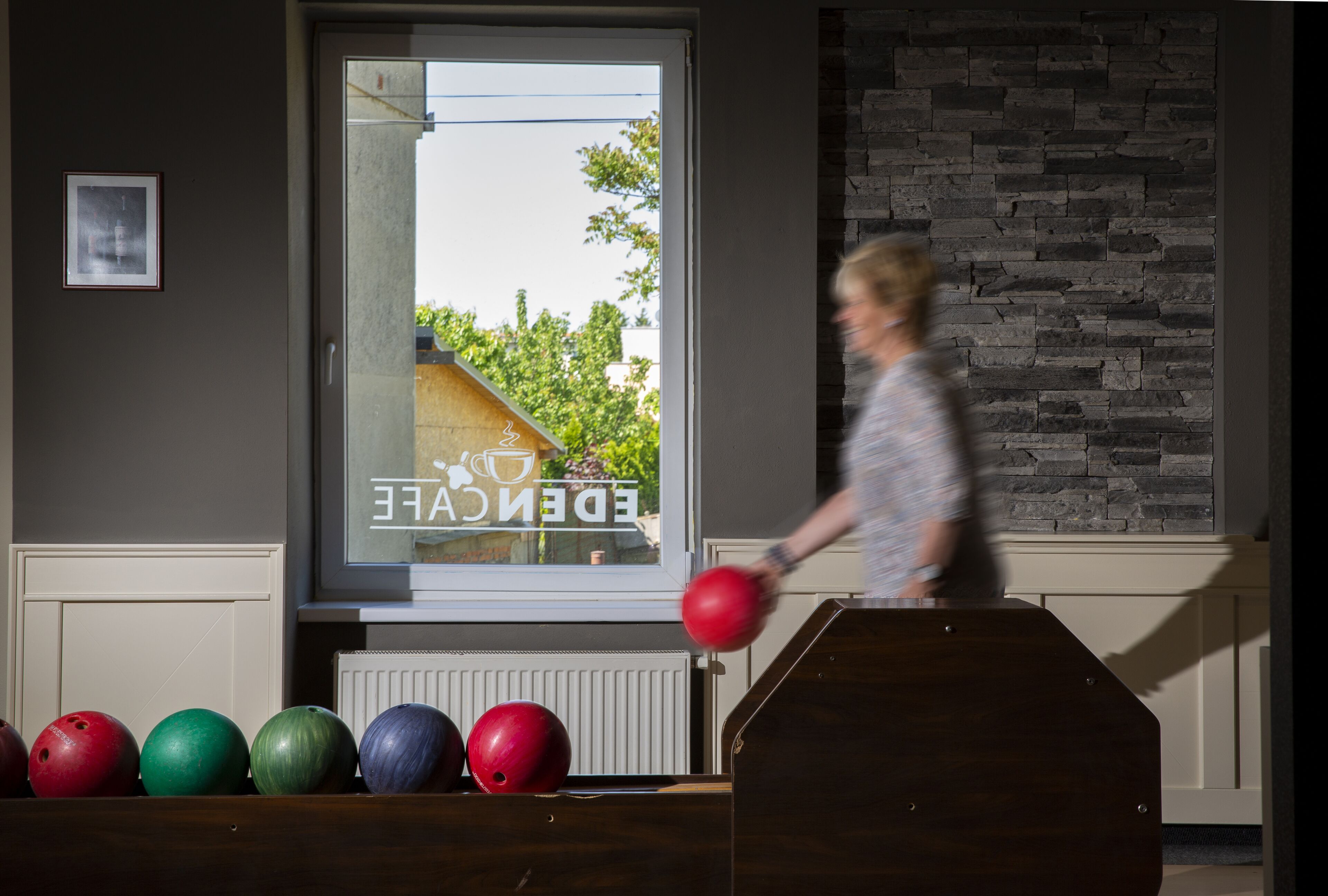 A bowling alley with a stone wall and a window with a view of greenery.