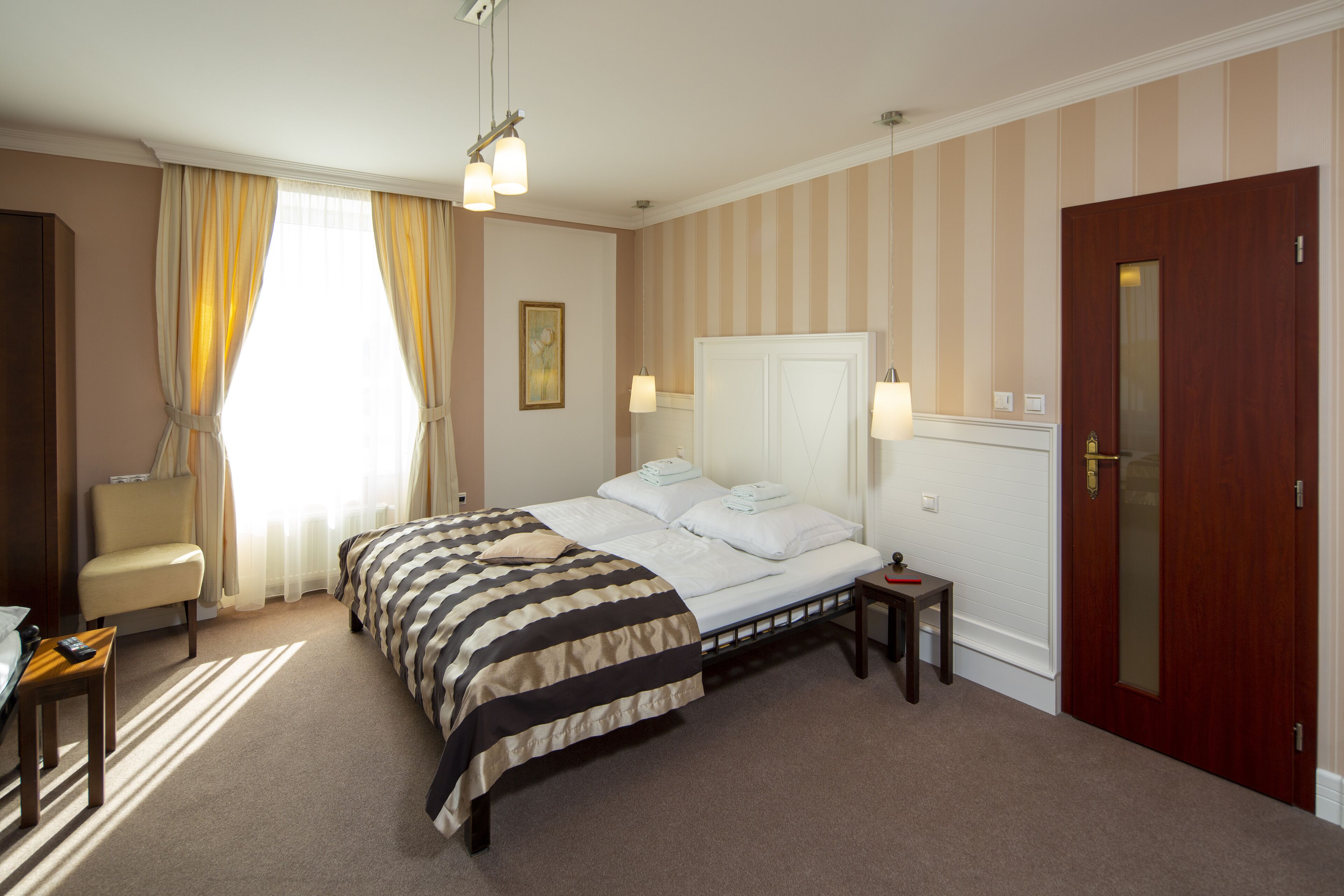 A hotel room with a large bed, a chair, a desk, and a door.