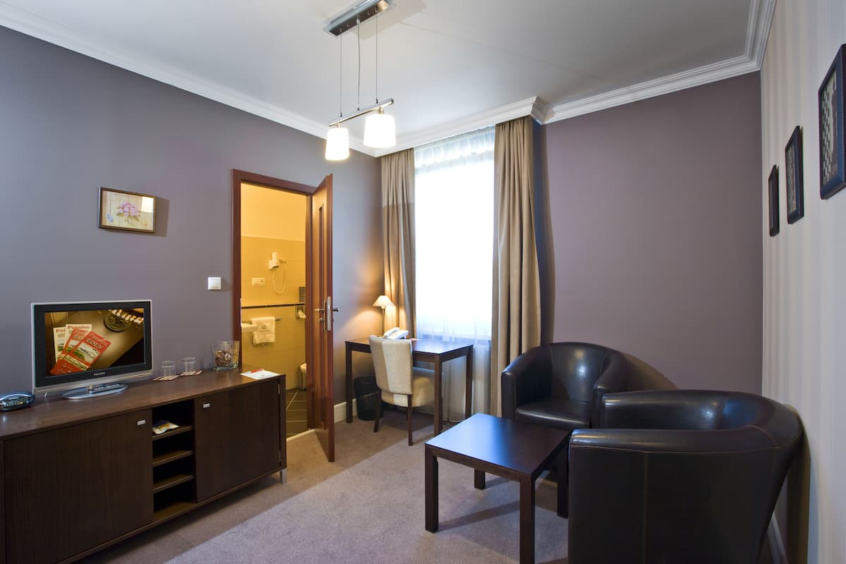 A hotel room with a flat-screen TV, a wooden desk, a leather armchair, and a sofa.