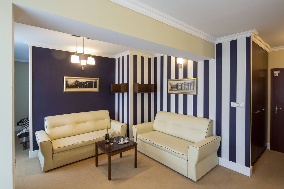 A living room with two cream-colored sofas, a wooden coffee table, and striped wallpaper.