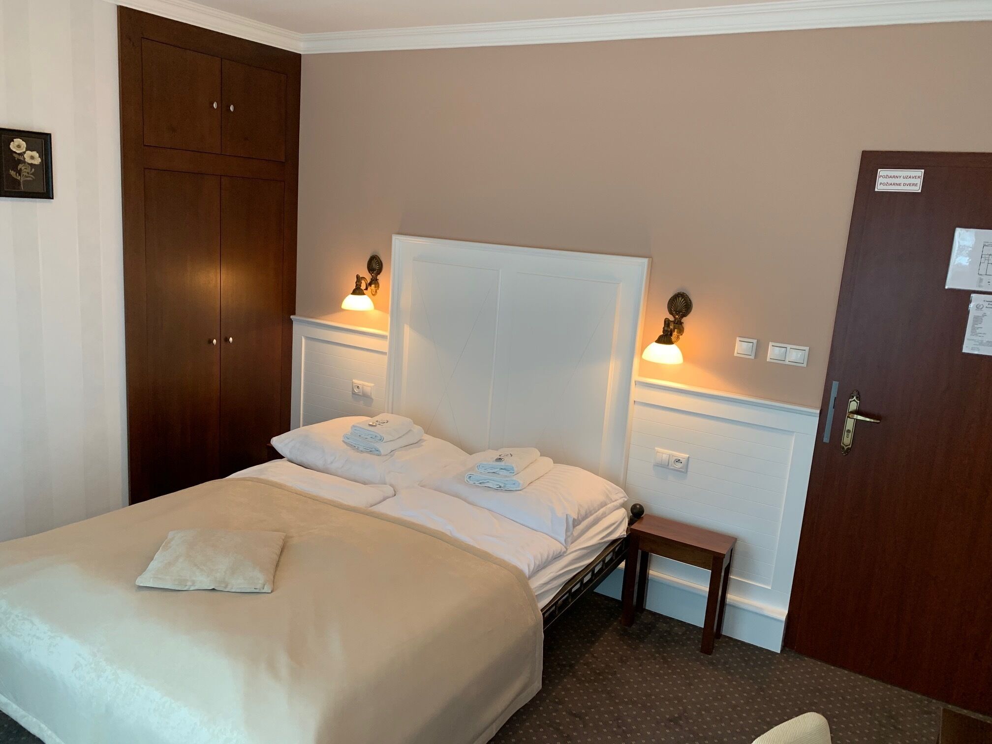 Una habitación de hotel con una cama grande, dos mesitas de noche, un armario de madera y una puerta con un letrero.