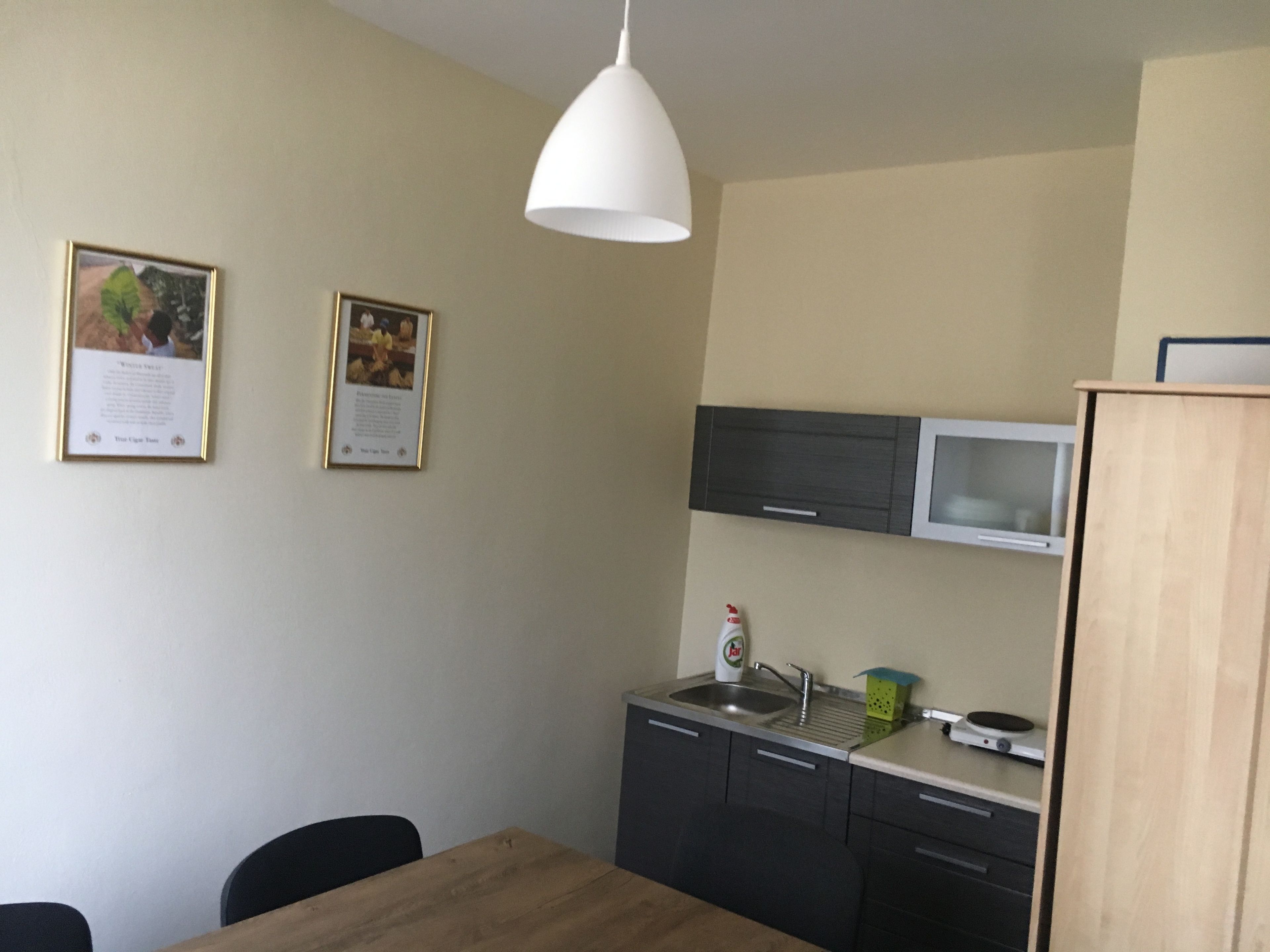 A compact kitchen with a wooden table, two chairs, a white pendant light, and a microwave above a dark cabinet.