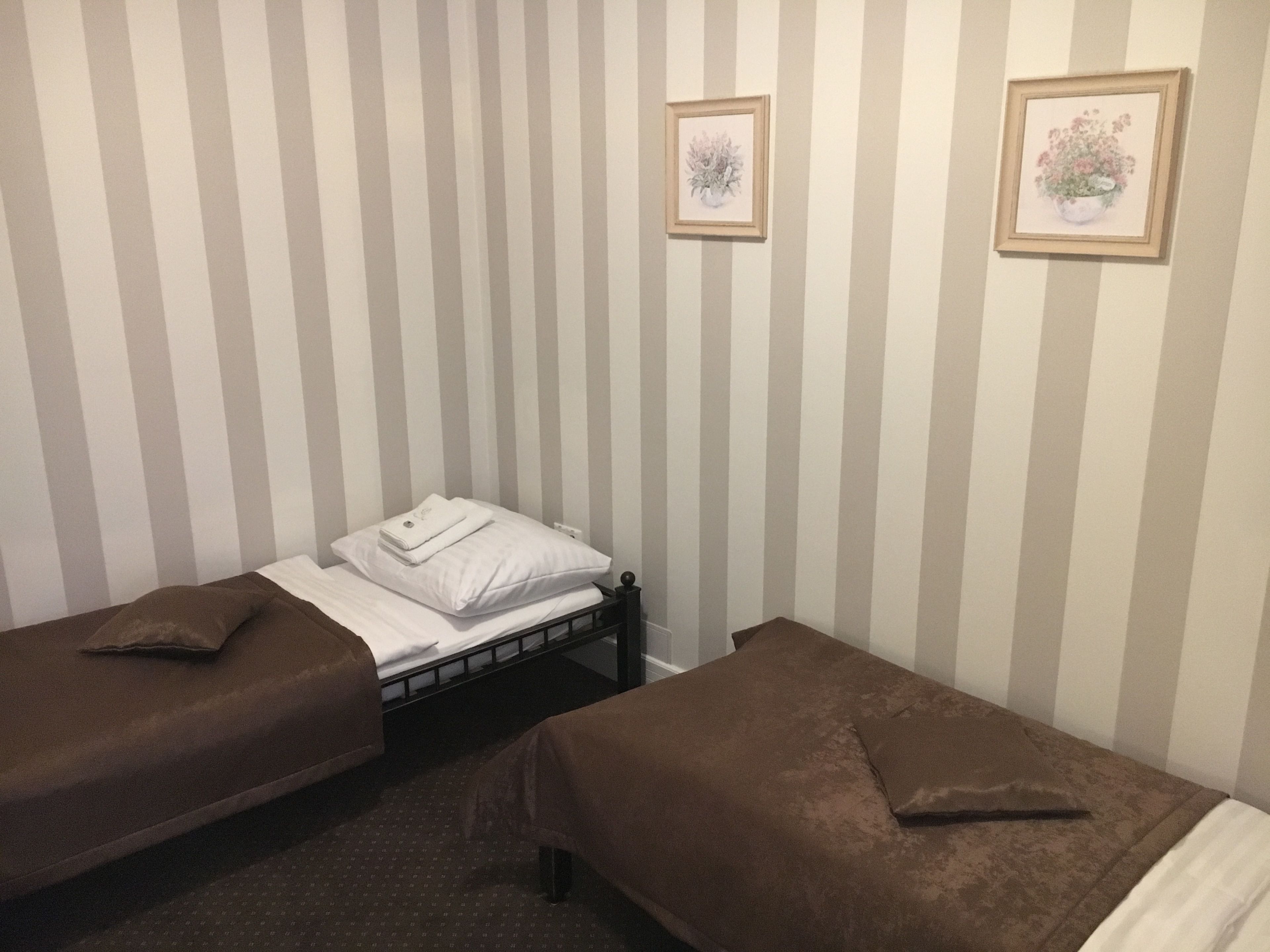 A room with two single beds, each with a brown cover and pillows, against a wall with vertical stripes. There are two framed pictures on the wall, one above the other.