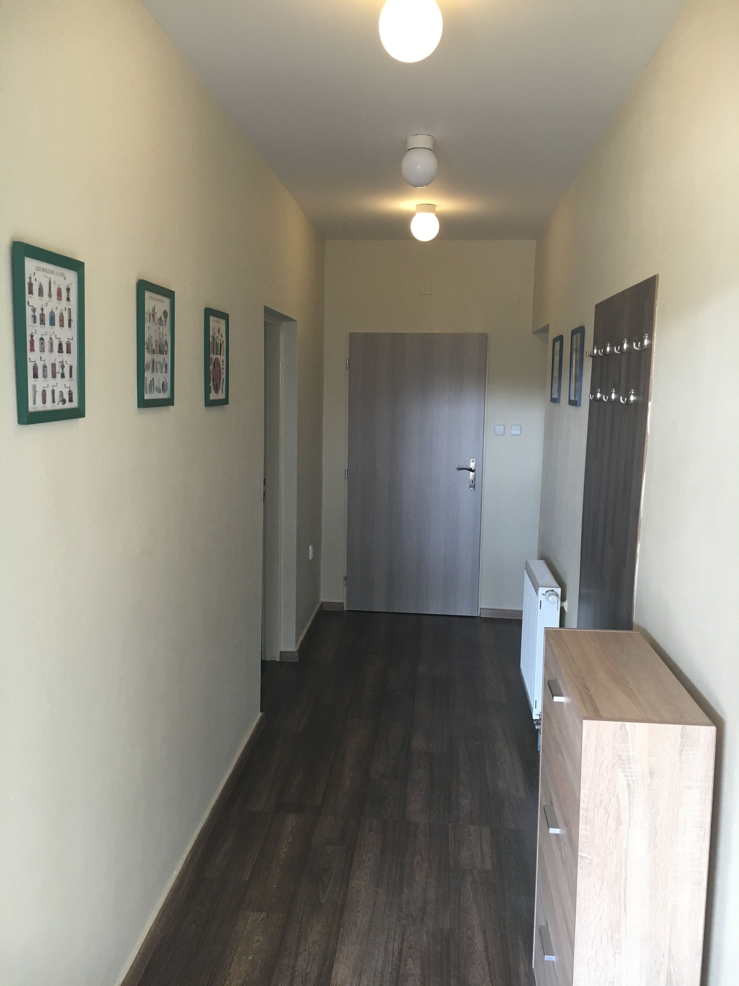 A hallway with a wooden floor, a door at the end, and three framed pictures on the wall.