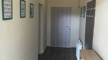 A hallway with a wooden floor, a door at the end, and three framed pictures on the wall.