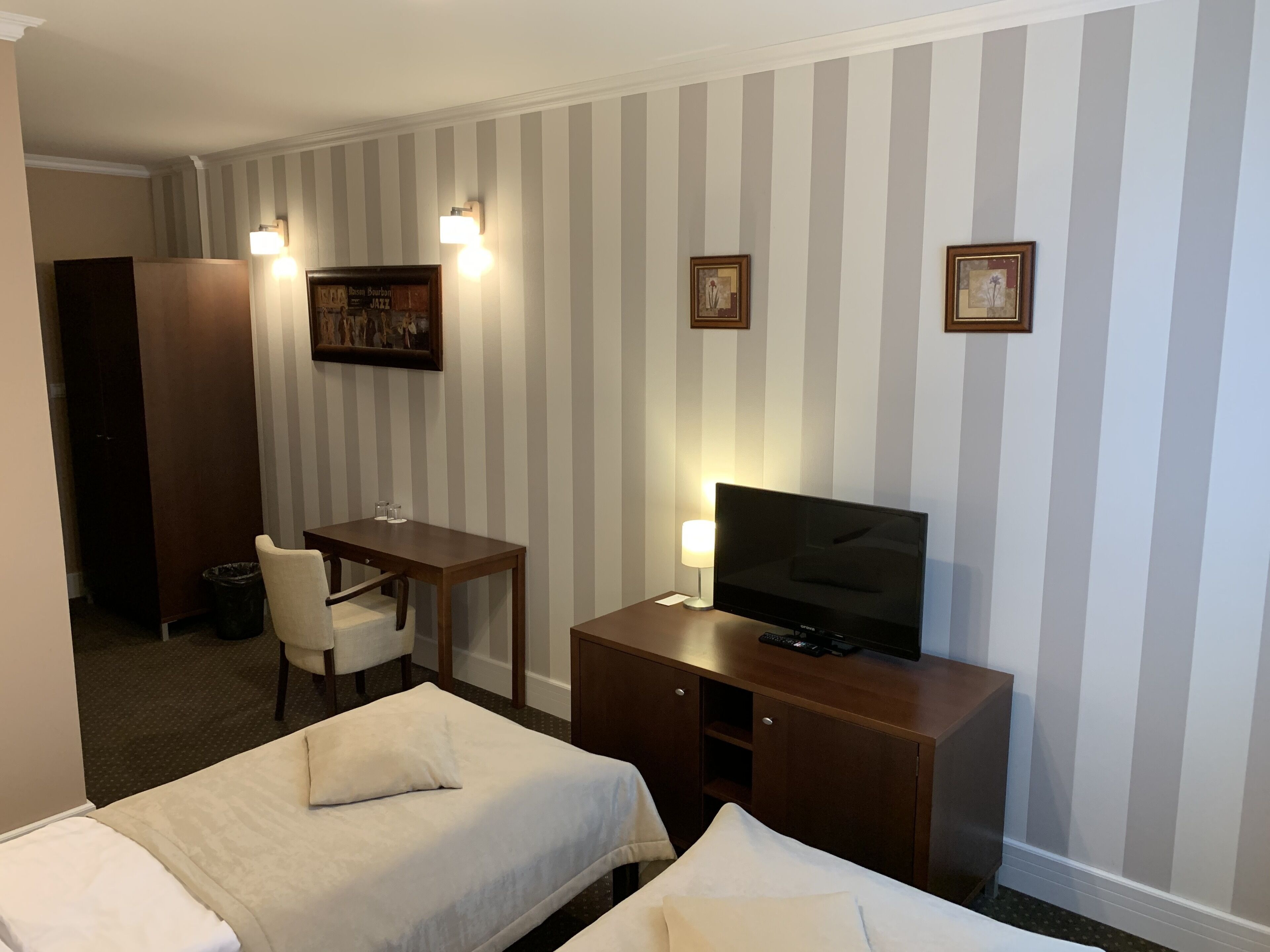 A hotel room with two beds, a desk with a chair, a TV, and two wall-mounted lights.