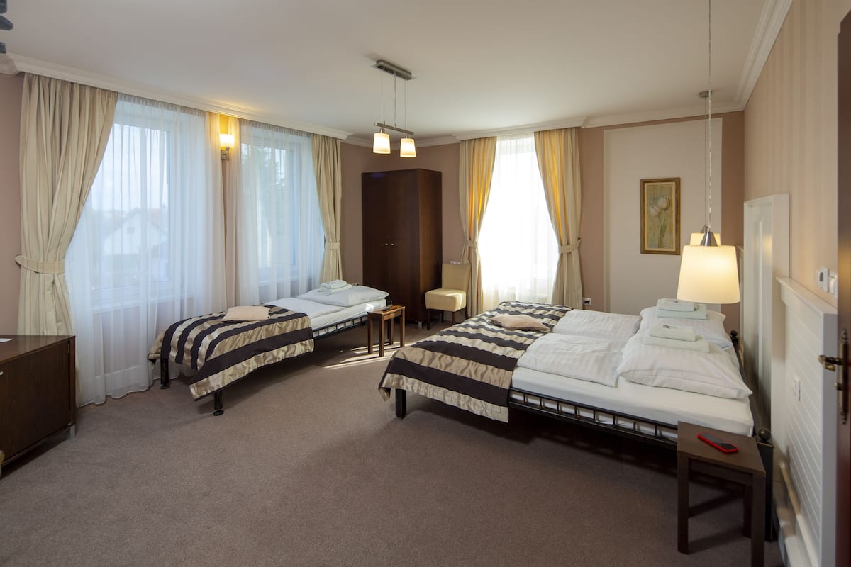 A hotel room with two beds, a small table, a chair, and a lamp.