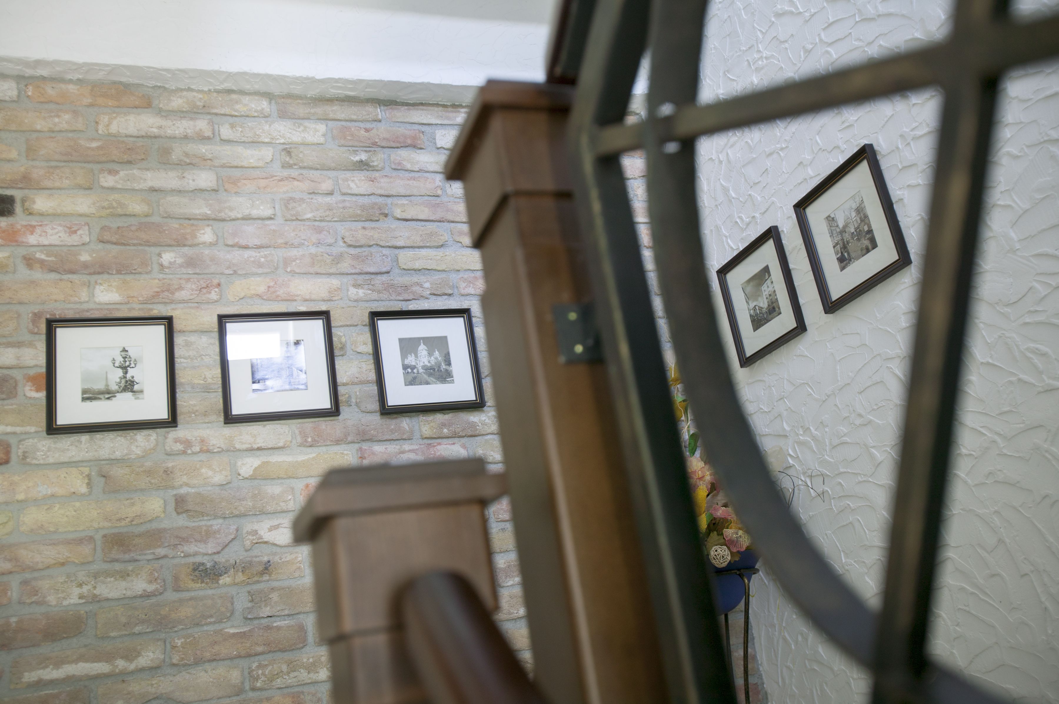 A brick wall with framed pictures and a wooden railing.
