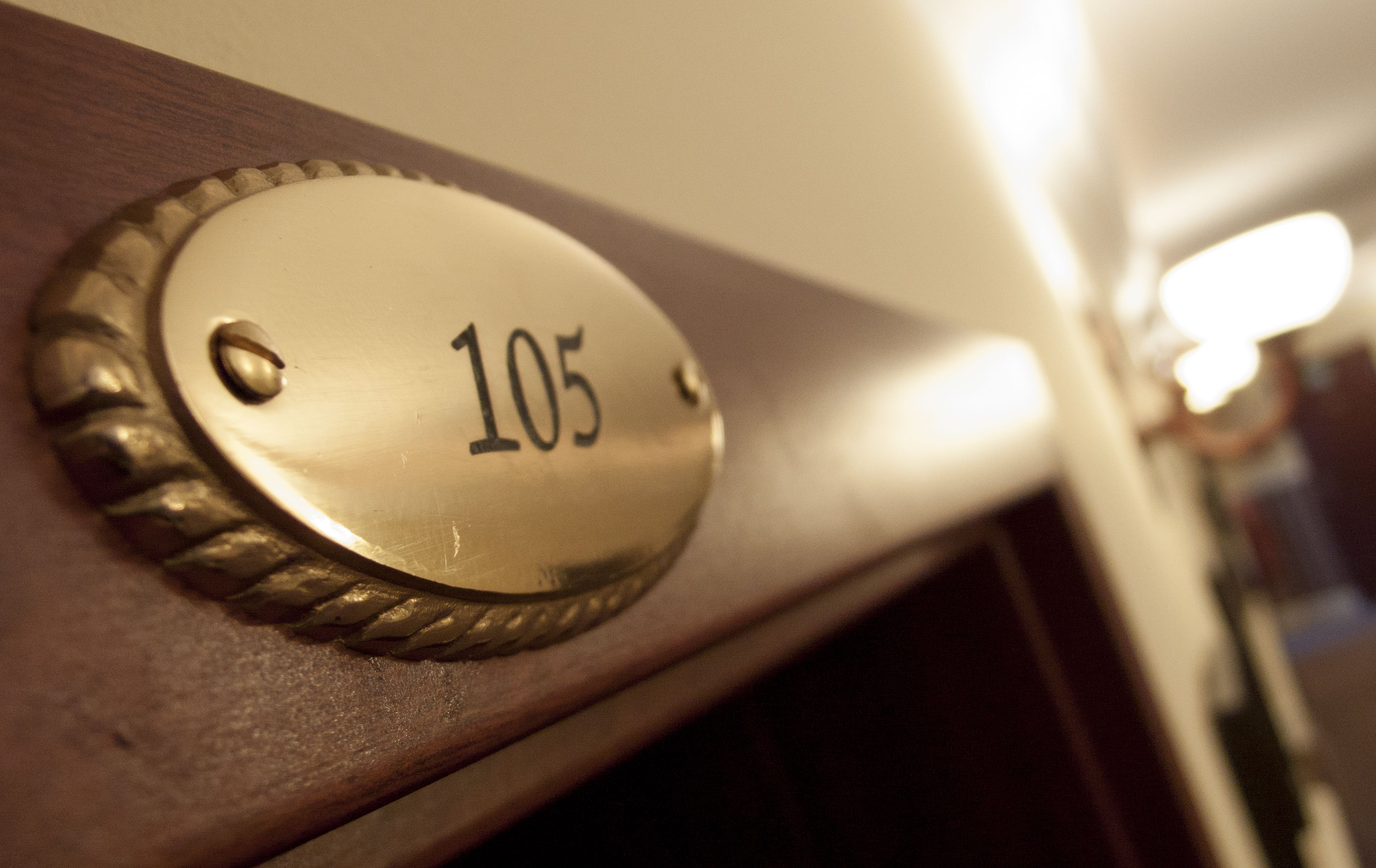 A brass doorplate with the number 105 on a wooden door.