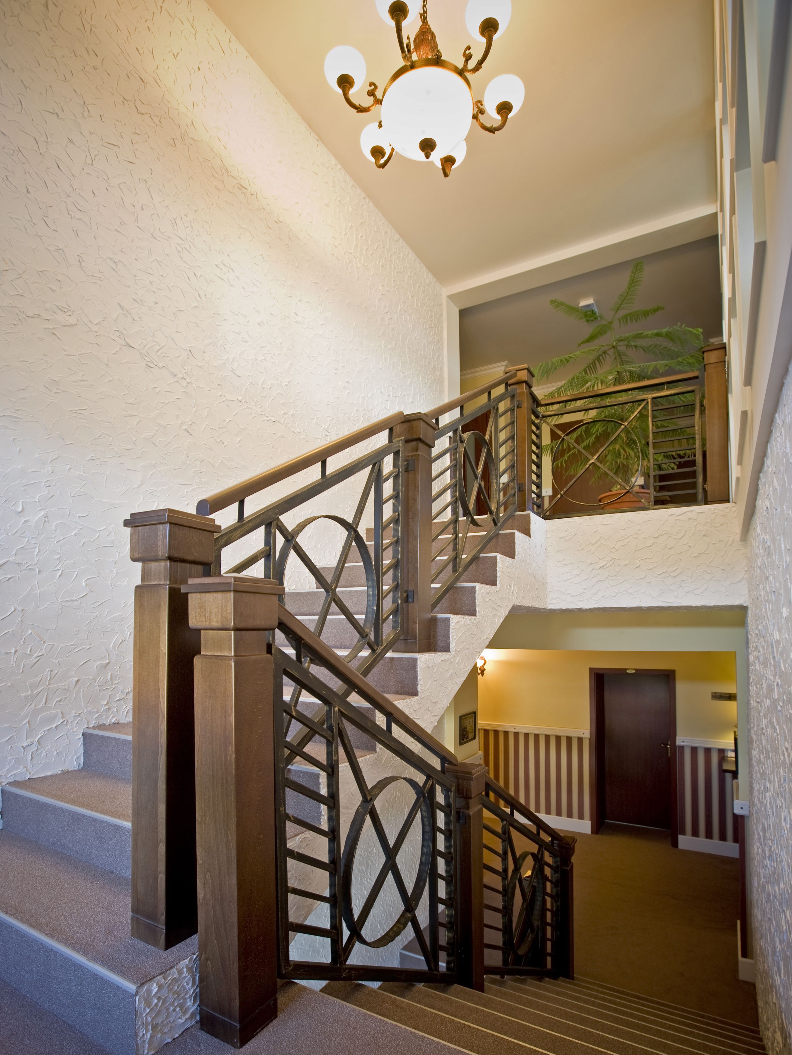 A staircase with a wrought iron railing, a chandelier, and a view of a balcony with a plant.