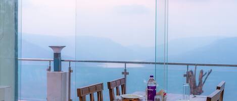 A dining table with chairs set for four, a bottle of Bailey's, and a salt shaker on a balcony overlooking a mountainous landscape.