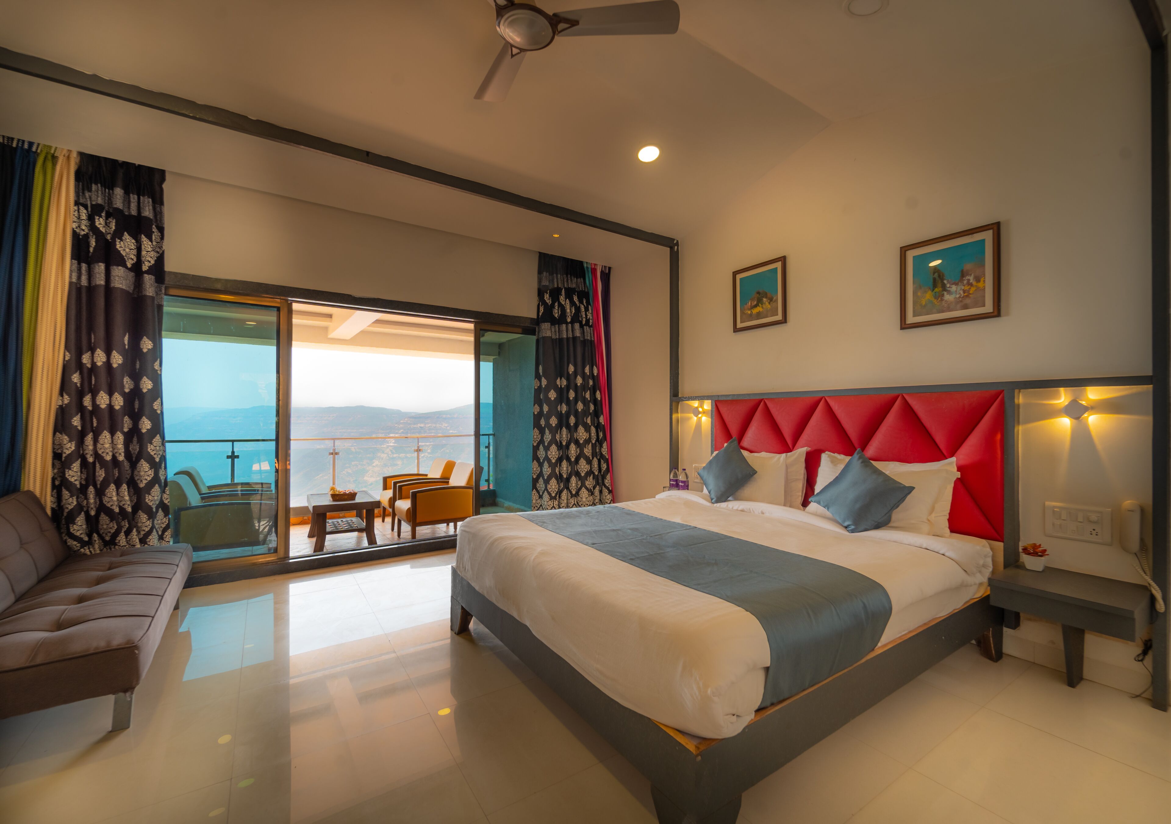 A modern hotel room with a large bed, a sofa, and a balcony with a view.