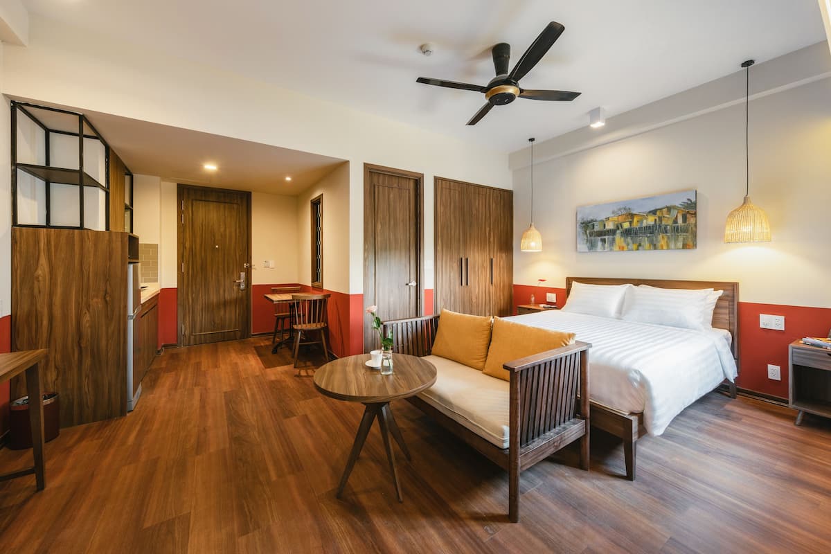 A hotel room with a bed, a sofa, a dining table, a ceiling fan, and a painting on the wall.