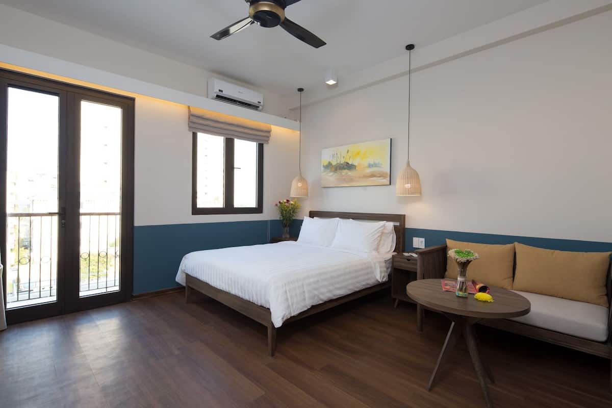 A bedroom with a bed, a sofa, a small table, a ceiling fan, and a window with blinds.