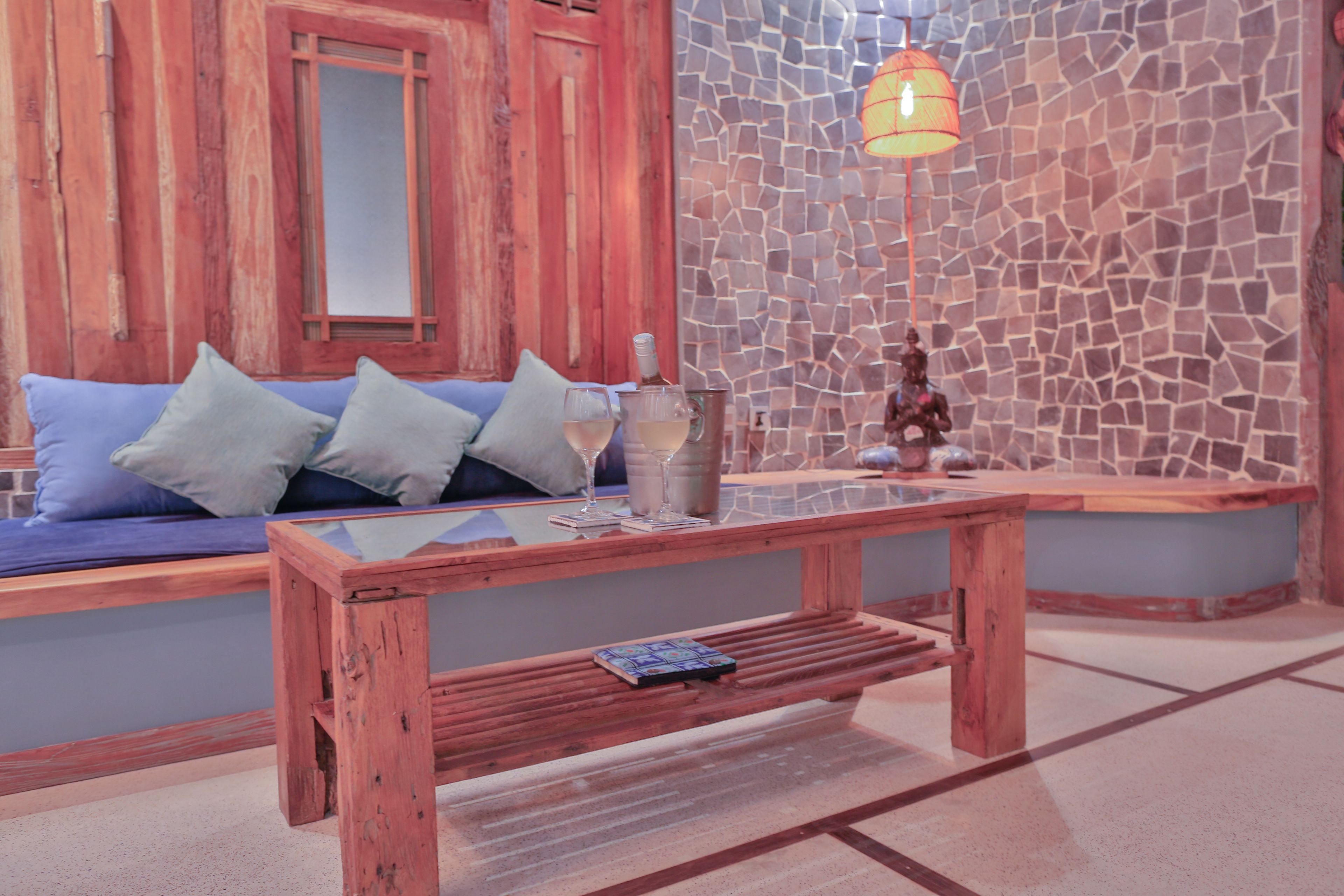 A wooden bench with a glass top, a small table with a book, and a wall with a mosaic pattern.