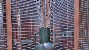 Un grand vase orné de branches, placé dans une pièce dont les murs sont recouverts de lambris en bois et où l'on trouve des stores métalliques.
