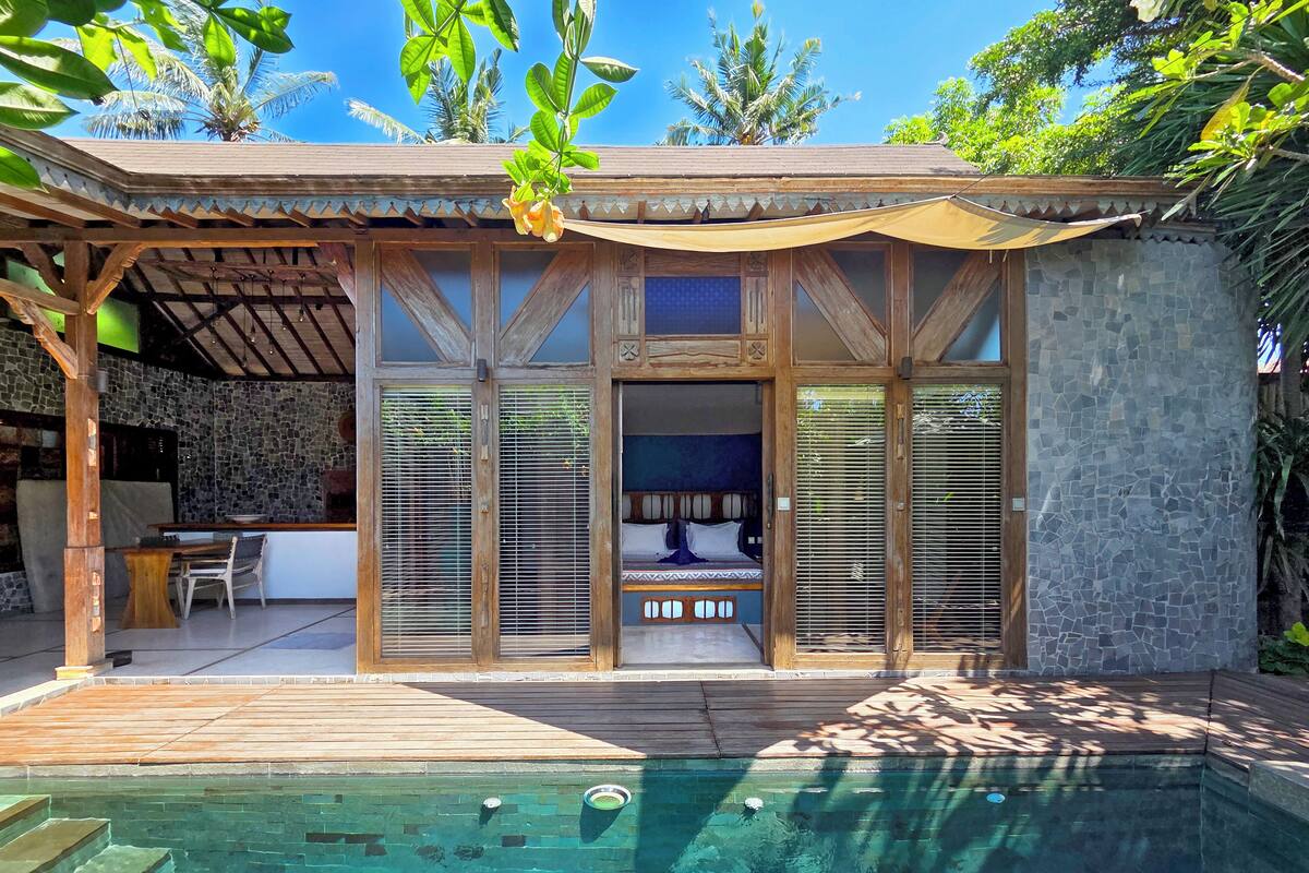 A modern villa with a pool, wooden deck, and a covered outdoor seating area.