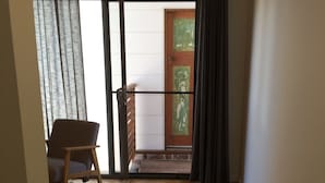 Una habitación con suelo de madera, una silla, un ventanal corredero que da a un balcón y vistas al exterior.