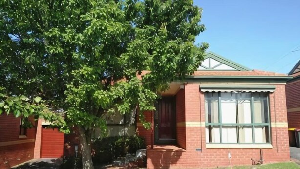 Un bâtiment en briques avec une grande fenêtre, un arbre devant et un ciel dégagé.