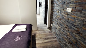 Una habitación de hotel con una cama, una toalla morada, una pared de ladrillo y suelo de madera.