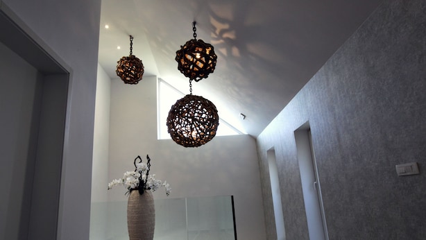 Un interior moderno con suelo de madera, un jarrón grande con flores blancas y tres lámparas colgantes esféricas.