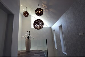 A modern interior with a wooden floor, a large vase with white flowers, and three hanging spherical light fixtures. - Apartments Art House (Škofljica)