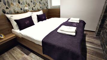 Una cama bien hecha con una manta y almohadas moradas, un cabecero de madera y un papel tapiz estampado.
