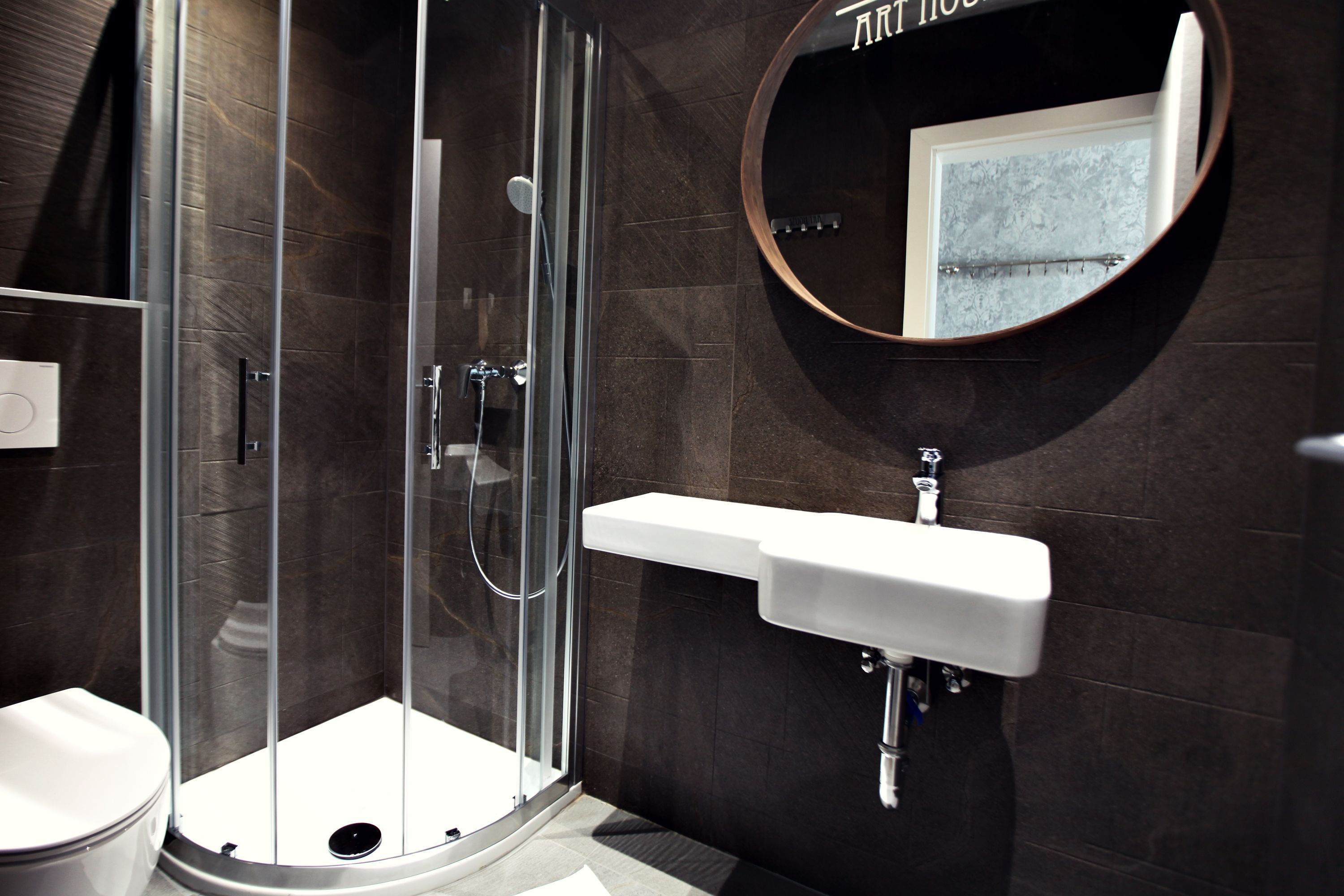 A modern bathroom with a glass-enclosed shower, a white sink, and a round mirror on the wall.