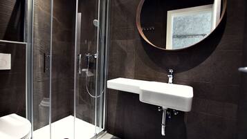 A modern bathroom with a glass-enclosed shower, a white sink, and a round mirror on the wall.