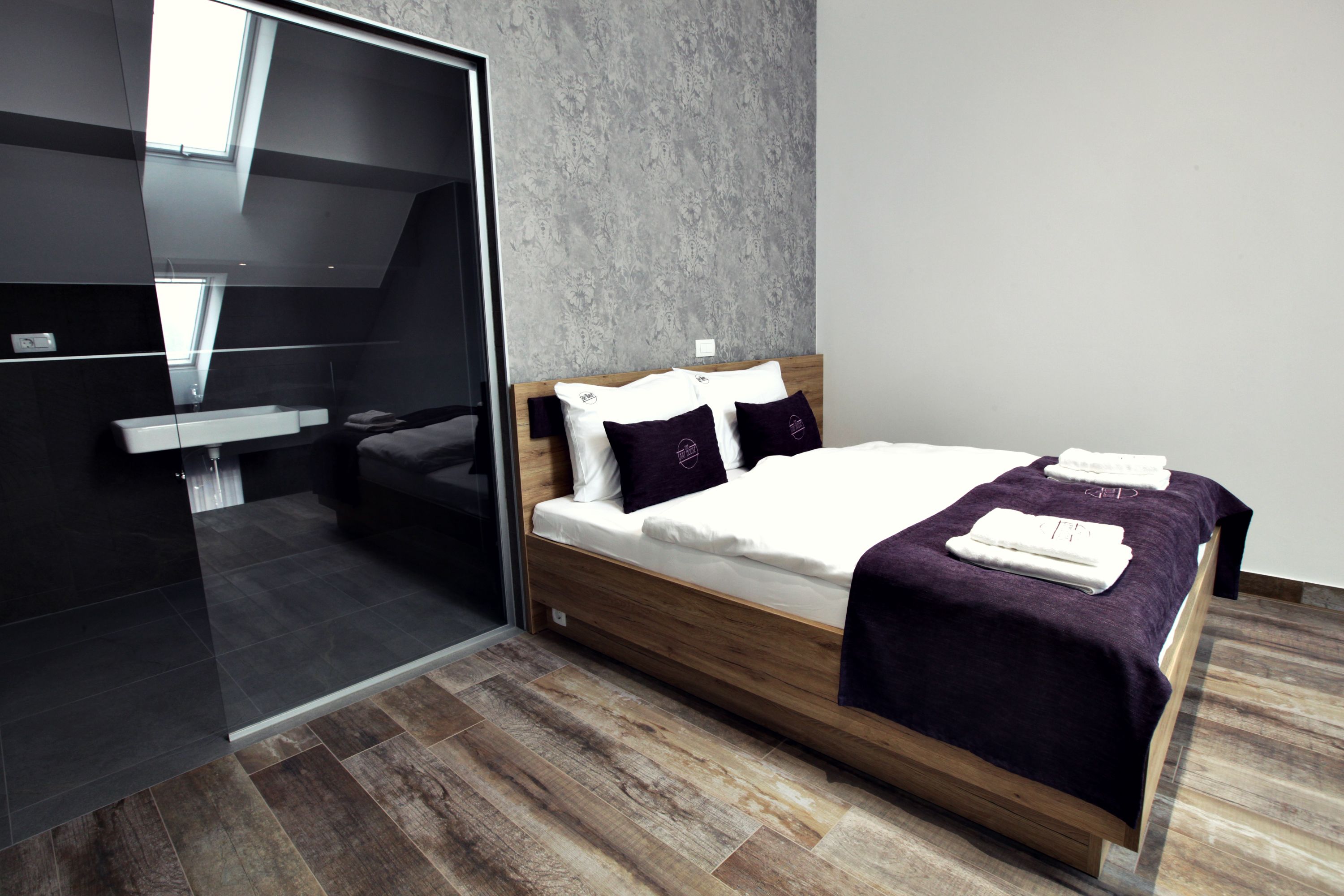 A modern bedroom with a wooden bed, a glass partition, and a grey textured wall.