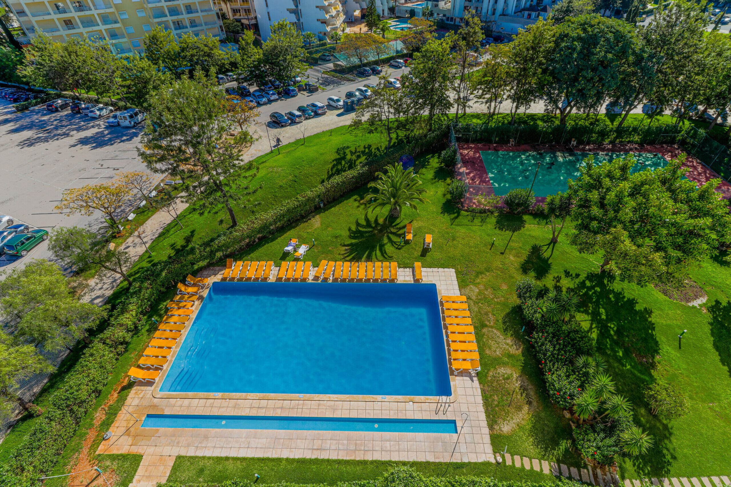 Vista aérea de un hotel con una gran piscina, tumbonas y un césped bien cuidado.