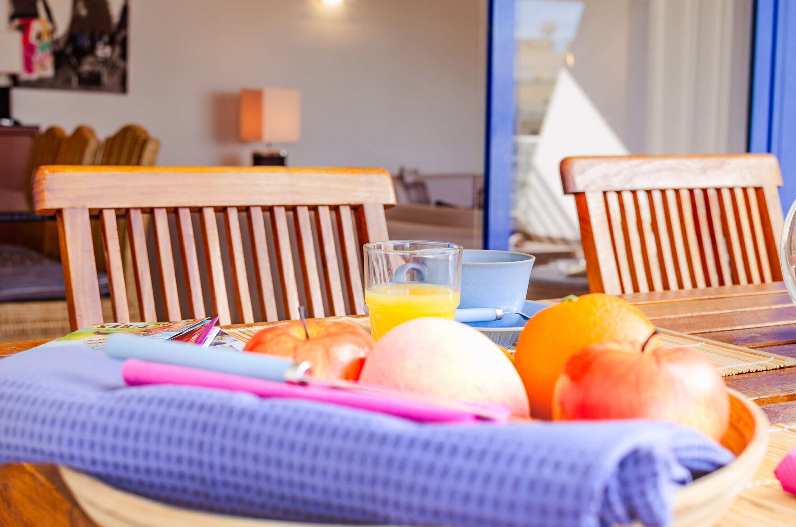 A breakfast table with a bowl of fruit, a glass of orange juice, and a notebook.