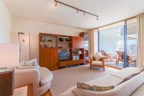 Un soggiorno moderno con divano, televisore, mobile TV in legno e un balcone con sedie.