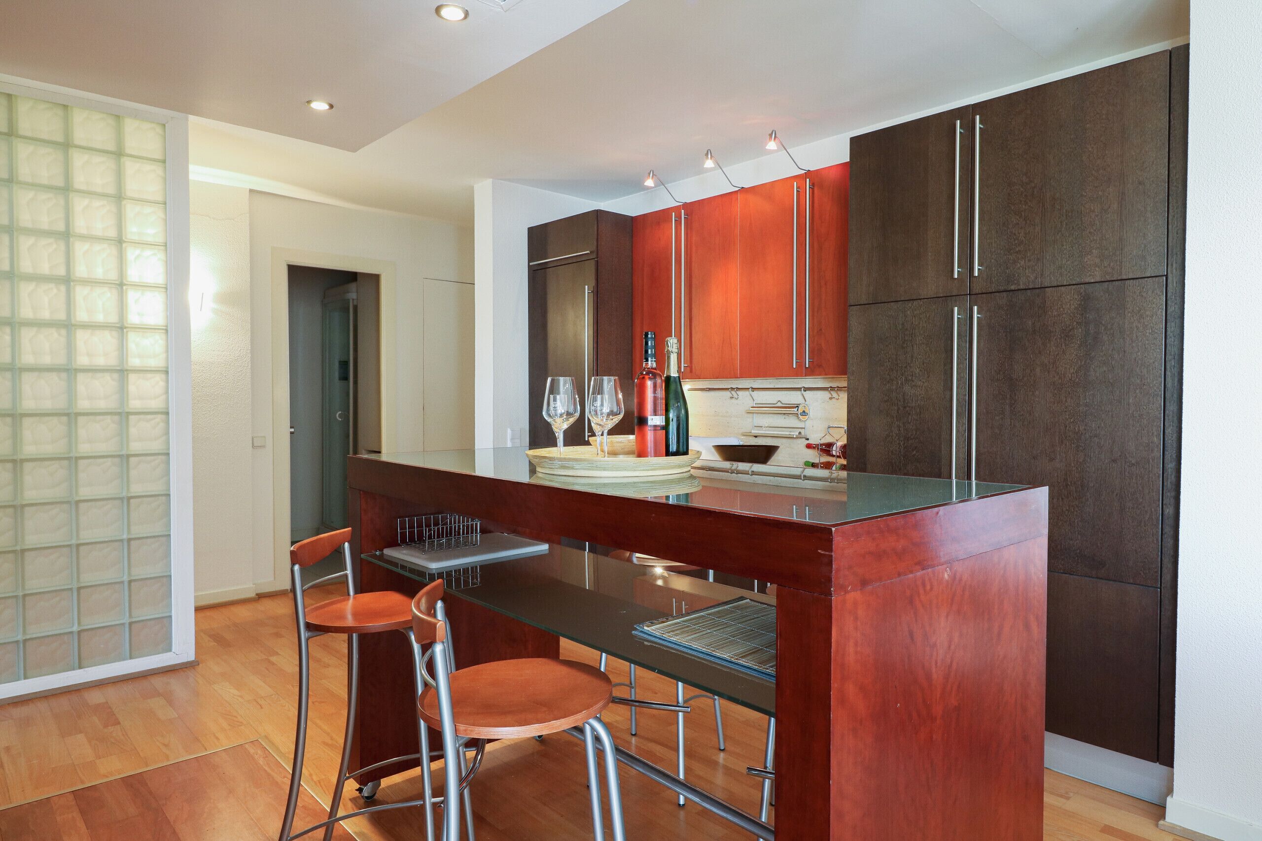 A modern kitchen with a central island, bar stools, and a wine bottle.
