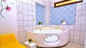 A bathroom with a large bathtub, a yellow chair, and a small table with flowers.